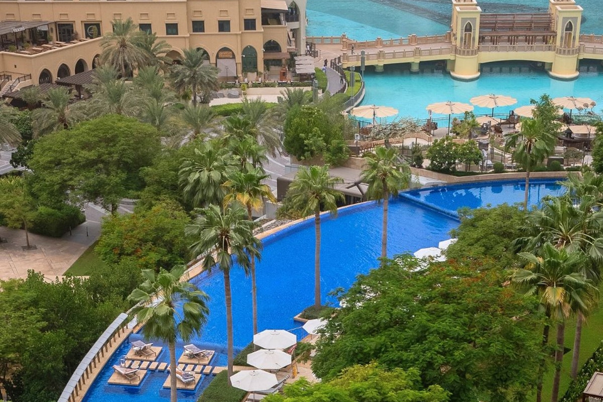 Aerial view of a resort with a blue pool surrounded by greenery and sun loungers.