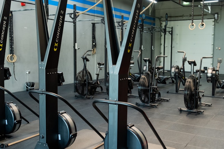 Gym setup featuring Concept2 rowing machines and bikes, along with various fitness equipment, in a modern, industrial-style gym with black tiled flooring