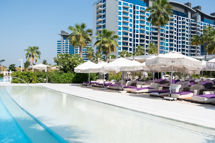In the background, a tall blue residential building contrasts with the clear blue sky, enhancing the resort-like atmosphere.