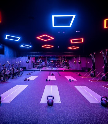 TruFusion Dubai Modern fitness studio with neon lighting, kettlebells, bikes, and workout mats.