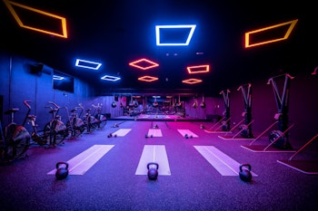 Modern fitness studio with neon lighting, kettlebells, bikes, and workout mats.