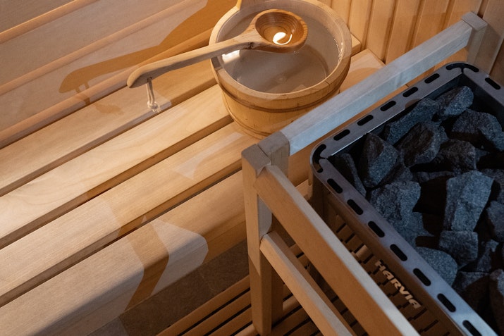 Close-up of a wooden sauna interior featuring a bucket with a ladle and heated stones, creating a classic sauna ambiance.