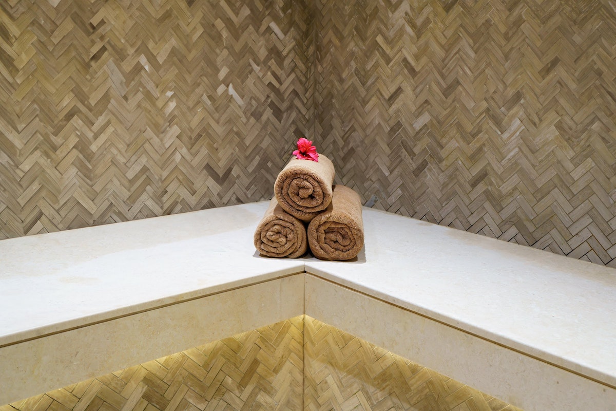 Rolled towels arranged on a marble spa bench with warm backlighting and textured wall tiles, creating a relaxing atmosphere.