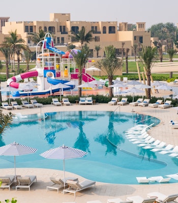 Sofitel Al Hamra Beach Resort An aerial view of a vibrant resort pool area featuring colorful water slides, lounge chairs, and palm trees, surrounded by resort buildings