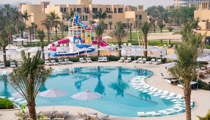 Sofitel Al Hamra Beach Resort An aerial view of a vibrant resort pool area featuring colorful water slides, lounge chairs, and palm trees, surrounded by resort buildings