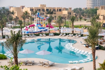 An aerial view of a vibrant resort pool area featuring colorful water slides, lounge chairs, and palm trees, surrounded by resort buildings
