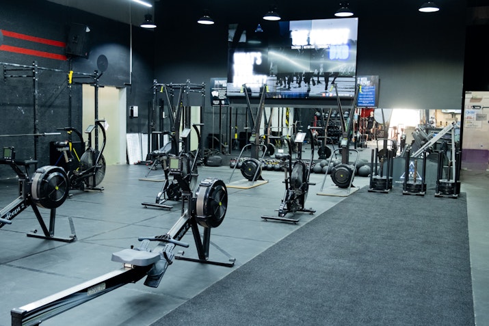 Gym area with rowers, air bikes, sled pushes, and various strength equipment, ideal for high-intensity circuit training and endurance exercises.