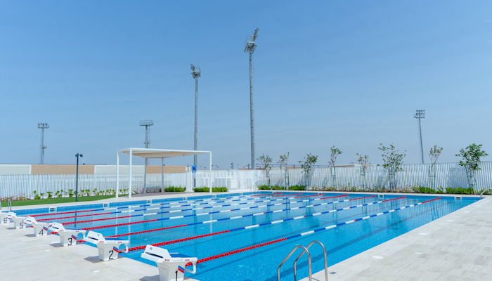 ABU DHABI 321 Sports An outdoor swimming pool with lanes, diving blocks, and clear blue skies.