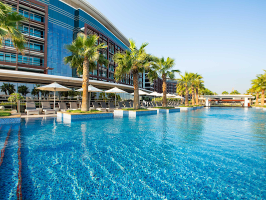 Outdoor pool with palm trees and a modern building in the background.