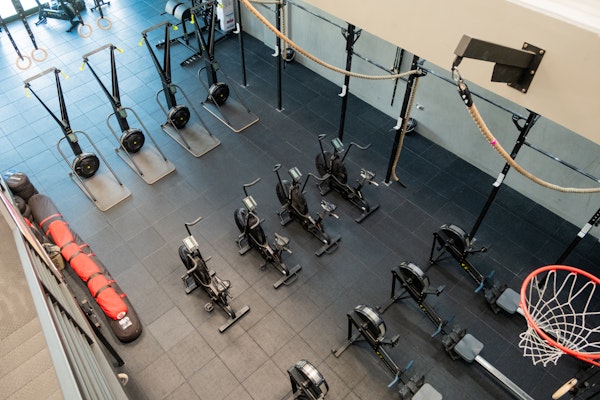 Aerial view of a gym with rowing machines, air bikes, ski ergs, and a wall rig with ropes, setup for cardio and strength workouts.