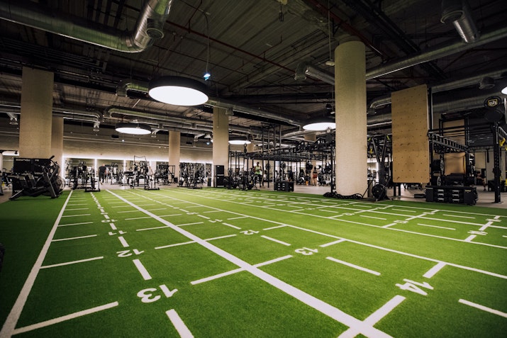 Indoor turf field, marked for functional fitness and agility training, surrounded by modern gym equipment.
