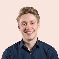 A young man with short blond hair and fair skin is smiling brightly. He is wearing a dark blue button-up shirt.