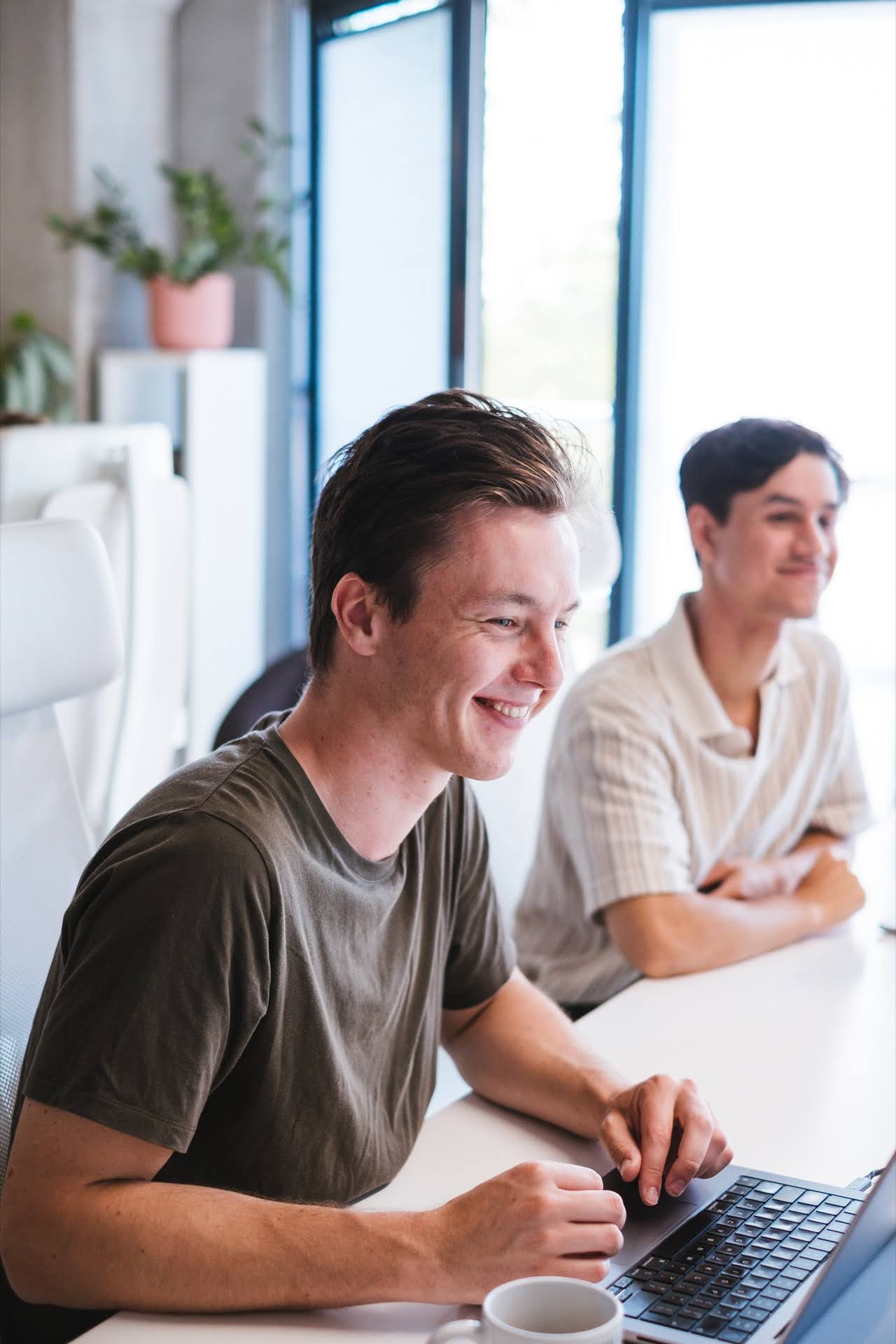 Two people sitting side by side at a white table, one of them is working on a laptop