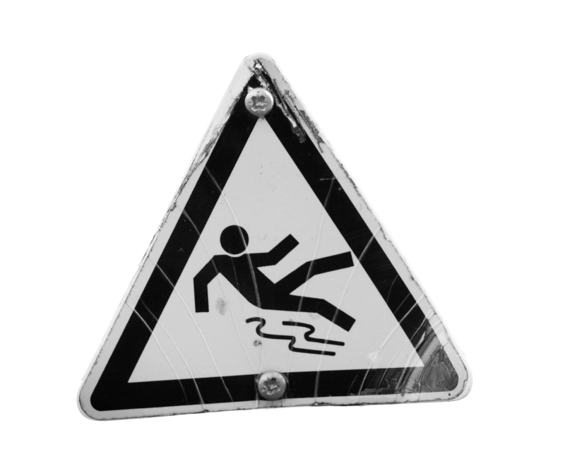 A triangular warning sign with a stick figure slipping, indicating a slippery surface hazard. The sign is worn and has visible scratches.