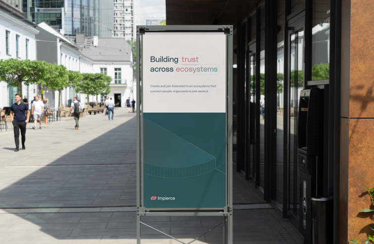 A sign outside a modern building reads, "Building trust across ecosystems. Create and join federated trust ecosystems that connect people, organizations and sectors." People walk in the background on a sunny day.