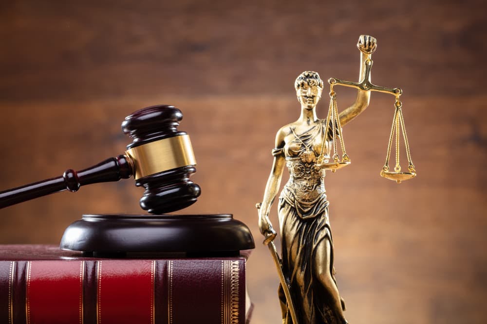 Close-up of Lady Justice statue with wooden gavel and law book, symbolizing justice and legal system