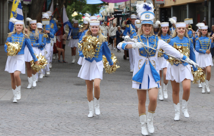 Ungdomsorkester i blåvit klädsel marscherar på en kullerstensgata