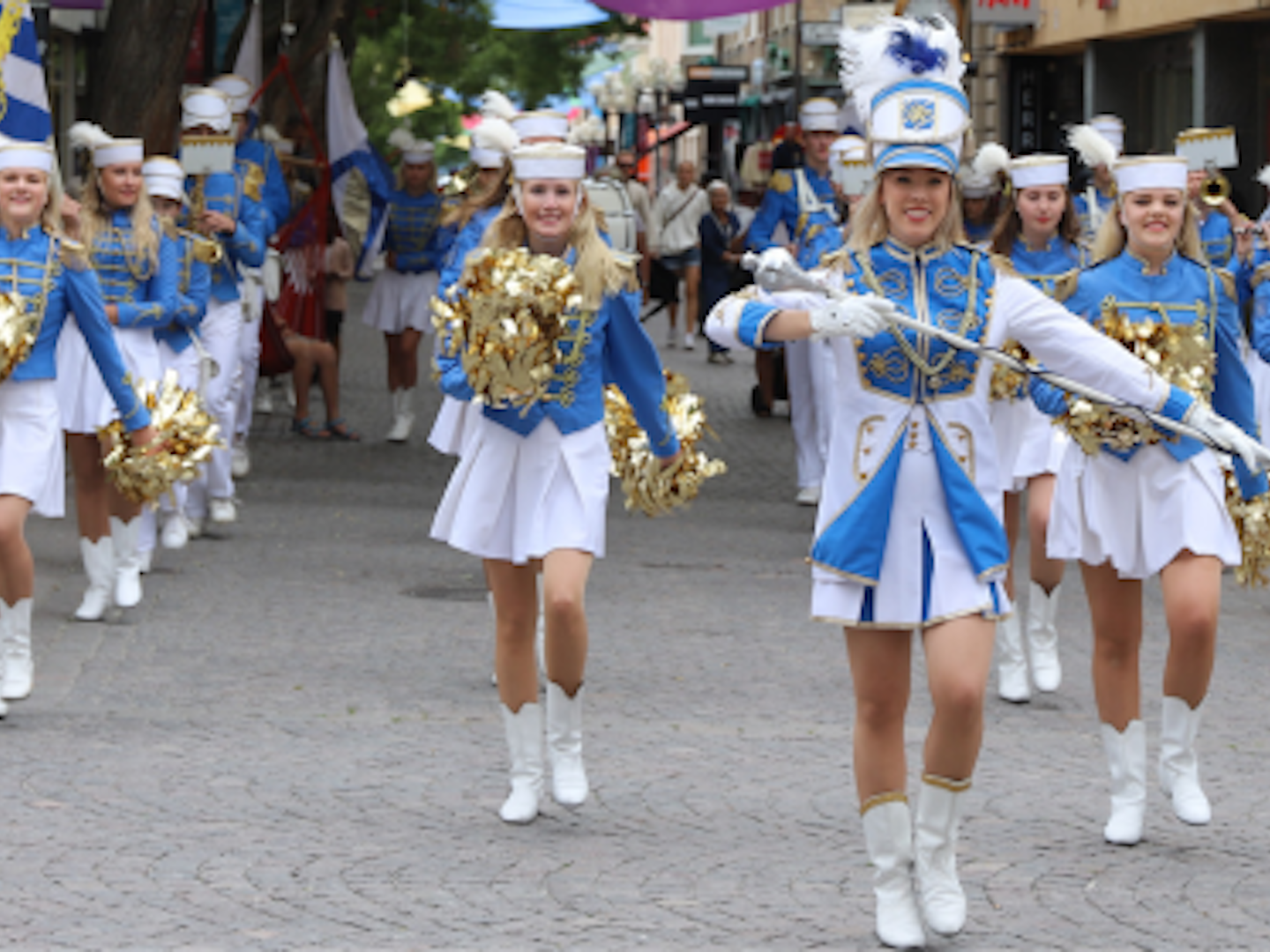 Ungdomsorkester i blåvit klädsel marscherar på en kullerstensgata
