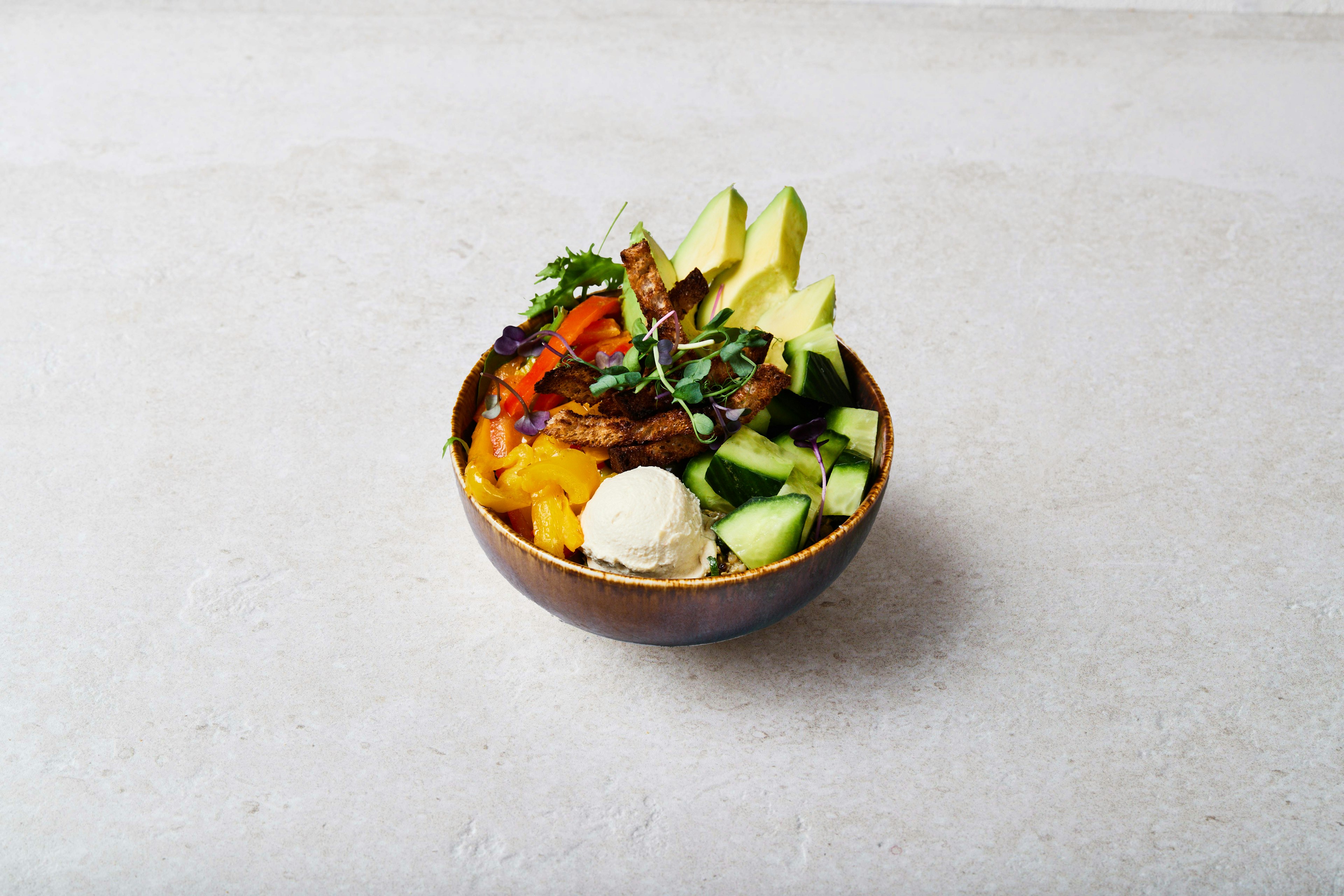 A close up picture of the seasonal vegetables bowl, a bowl with roasted peppers, avocado, quinoa tabbouleh, hummus, cucumber, mesclun, vegan vinaigrette, sprouted cress & homemade organic croutons