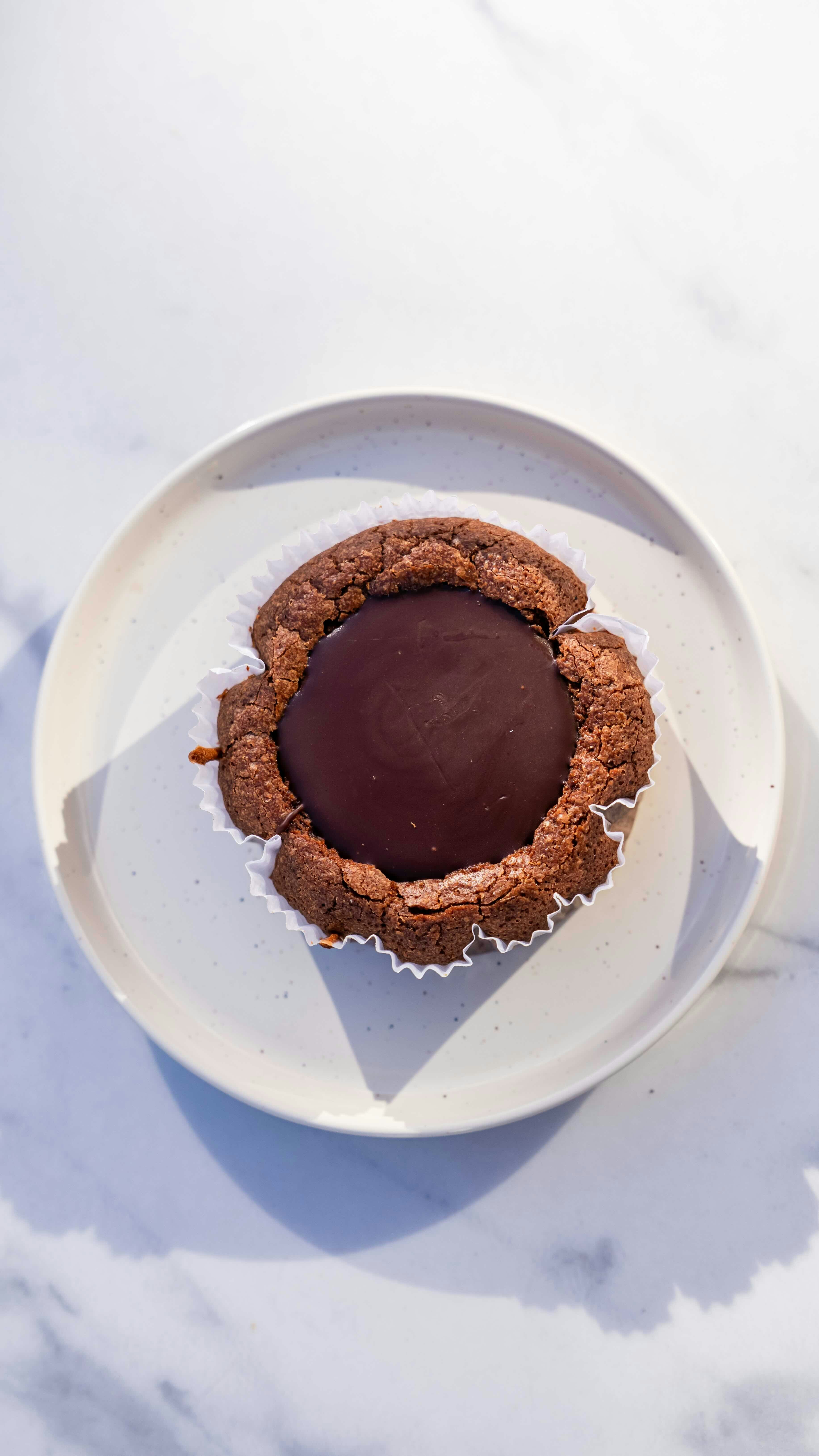 A chocolate tart with a glossy center sits on a white plate atop a light marble surface, photographed from above.