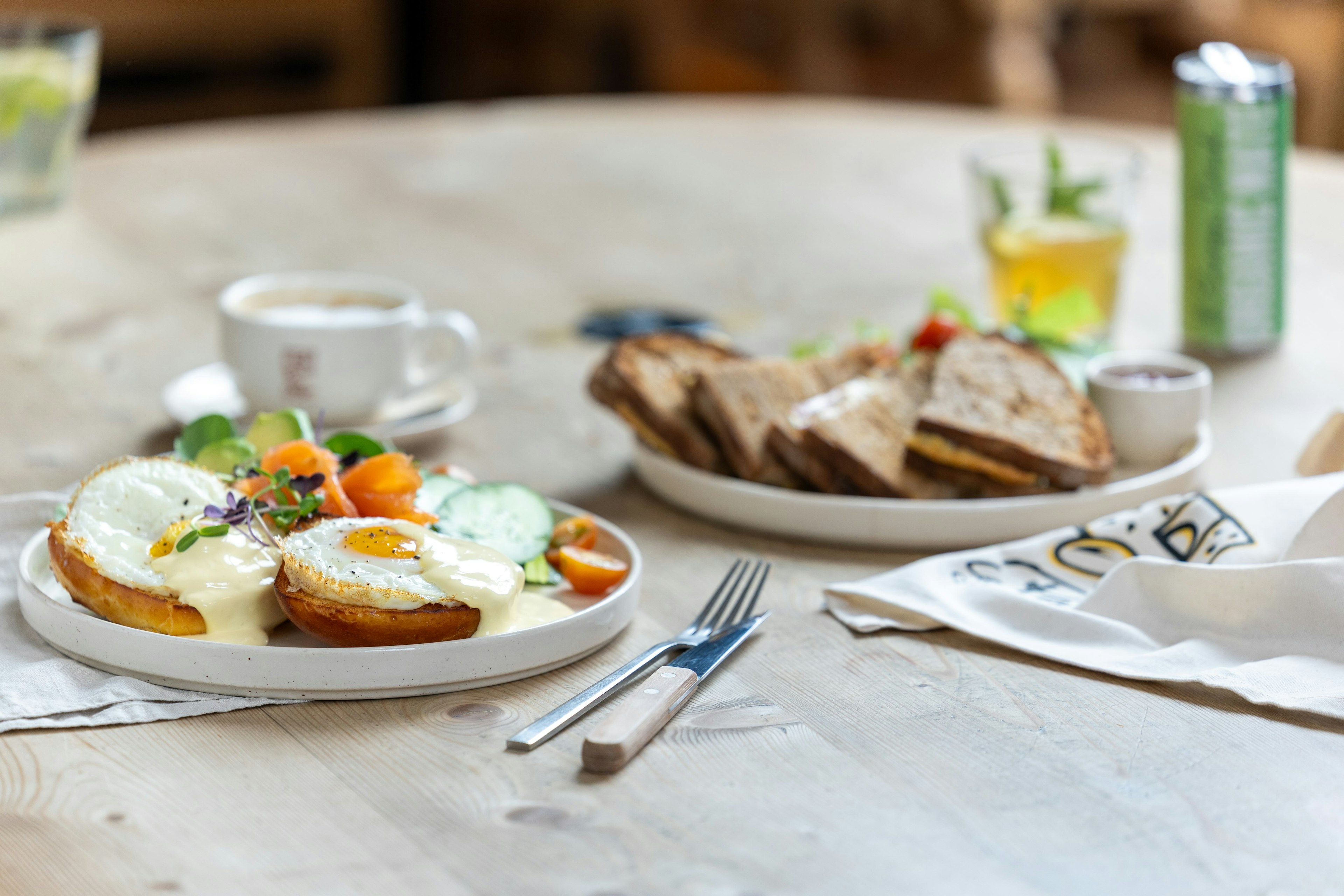 A picture of eggs benedict with salmon, a croque monsieur in the background and a coffee.