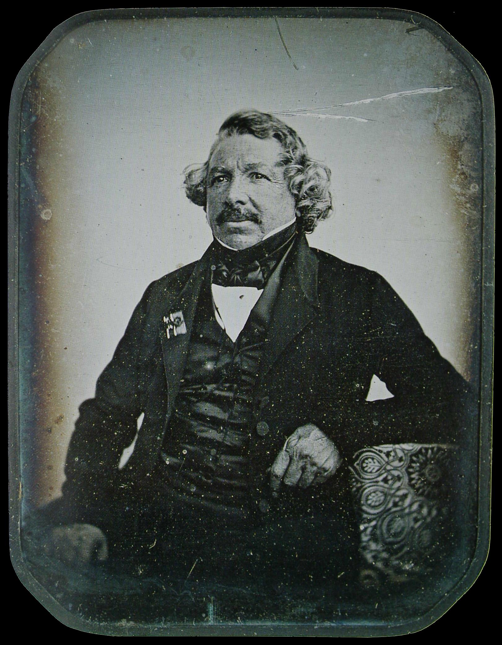 A black-and-white portrait of an older man seated, wearing a dark jacket and cravat, looking slightly to the side. The image shows the soft, slightly blurred texture typical of early daguerreotypes.