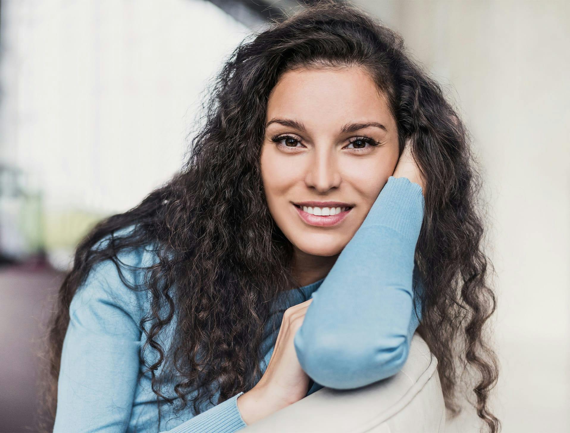 woman with curly brown hair resting her face along her arm