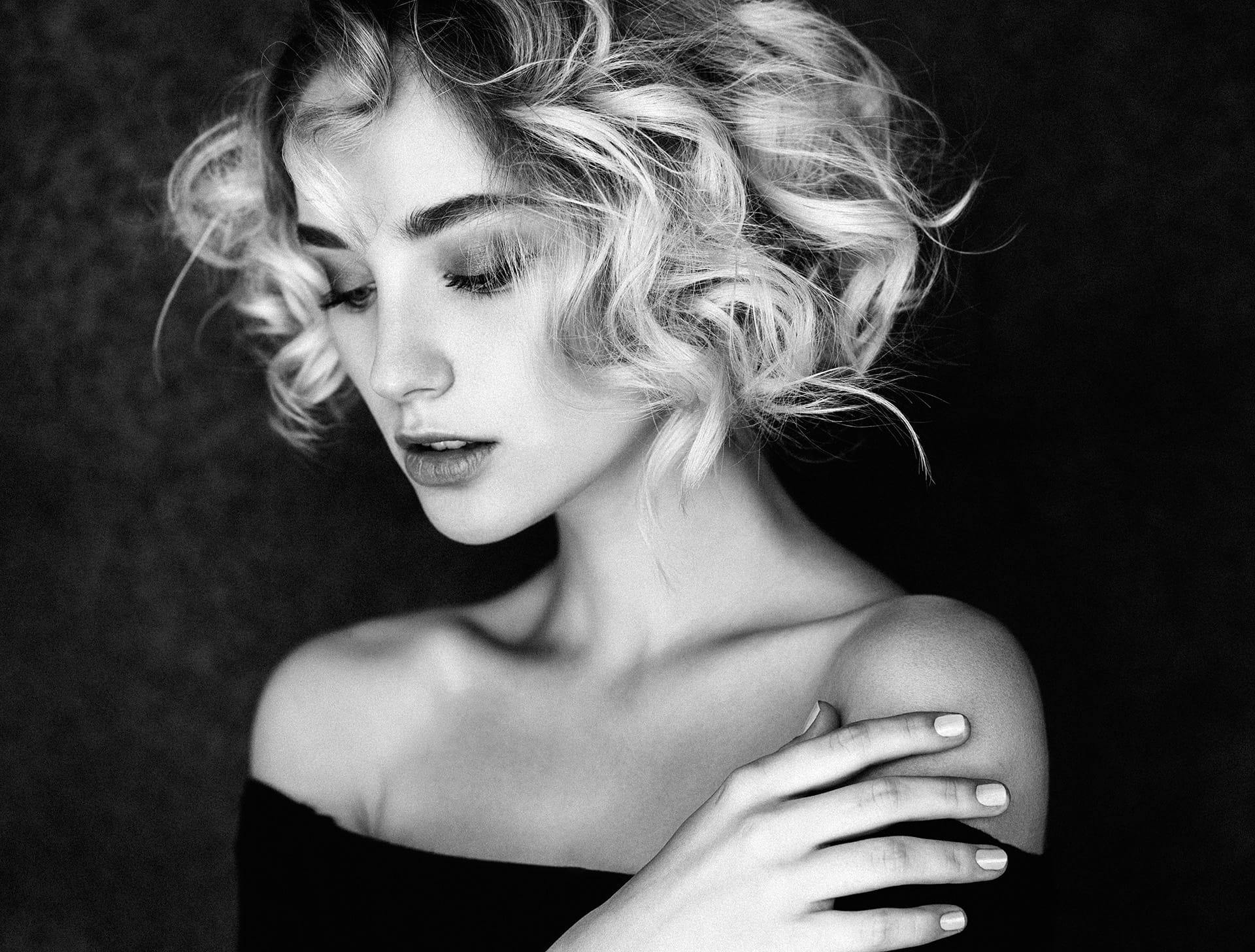 greyscale woman with curly short hair with hand on her shoulder