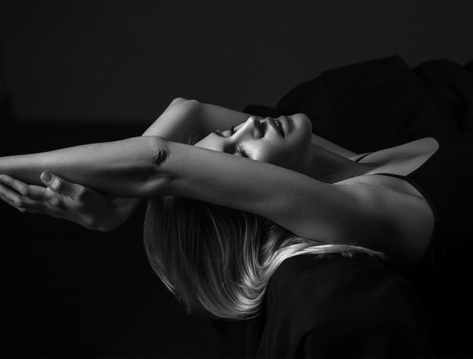 greyscale of woman laying on couch leaning off of it with her arms hanging off