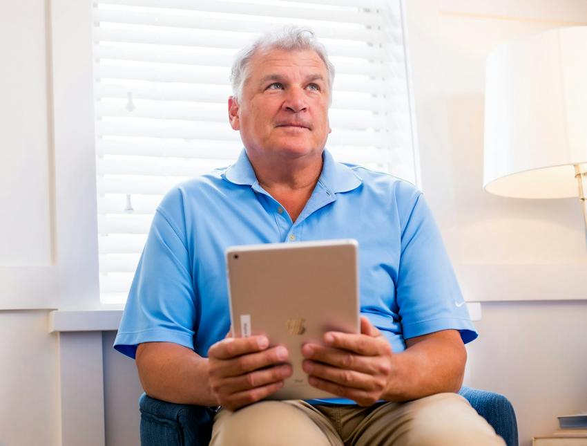 older man holding ipad while sitting in a chair