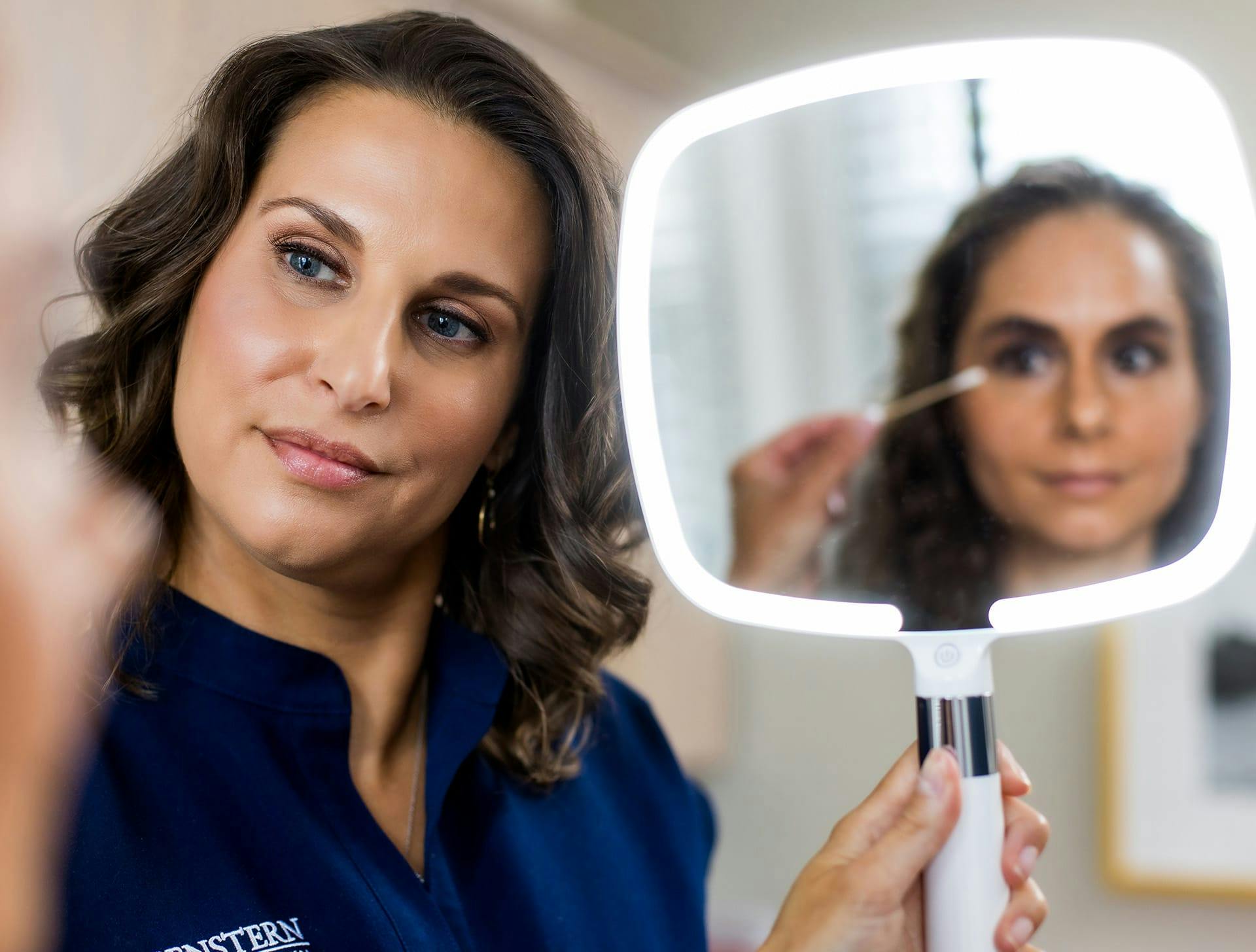 client looking into handheld mirror while nurse touching near her eye with q-tip