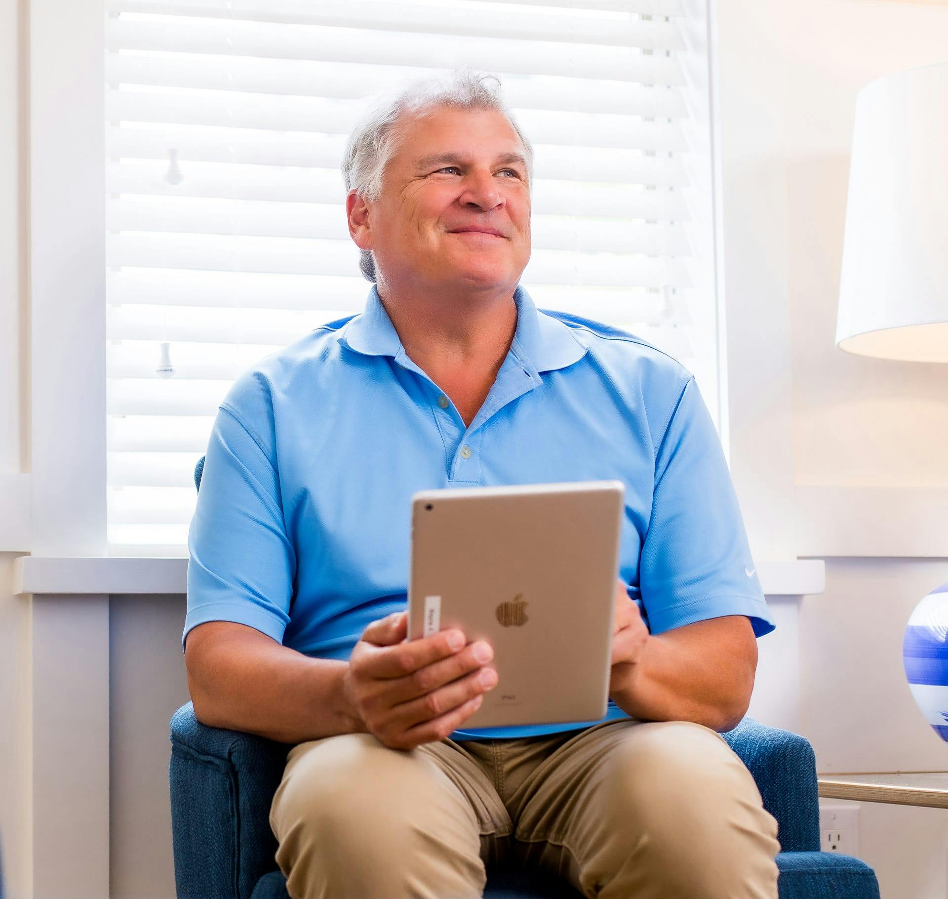 older man sitting down holding an ipad