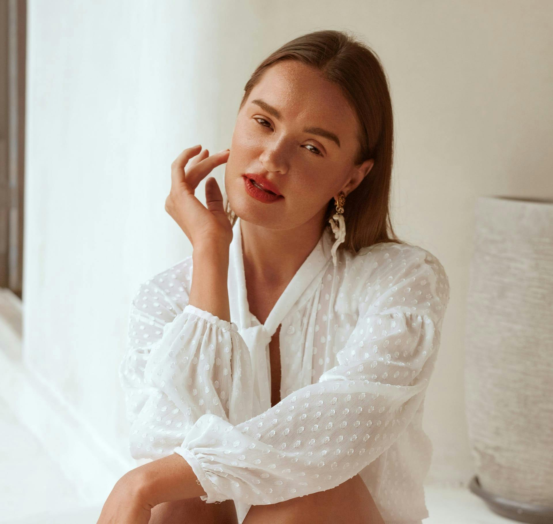woman with hand on her cheek sitting down with white top