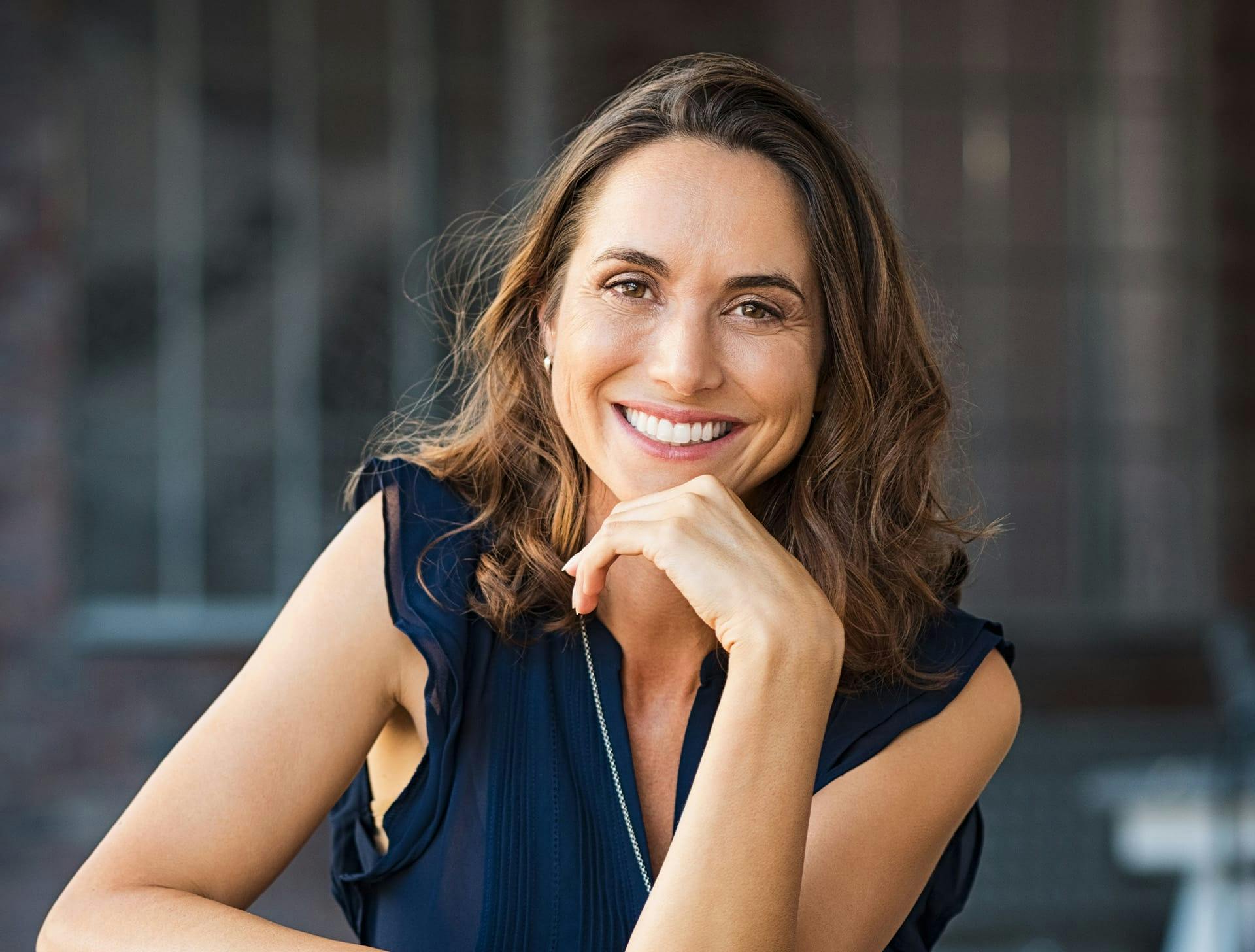 woman with brown curly hair smiling while touching her chin