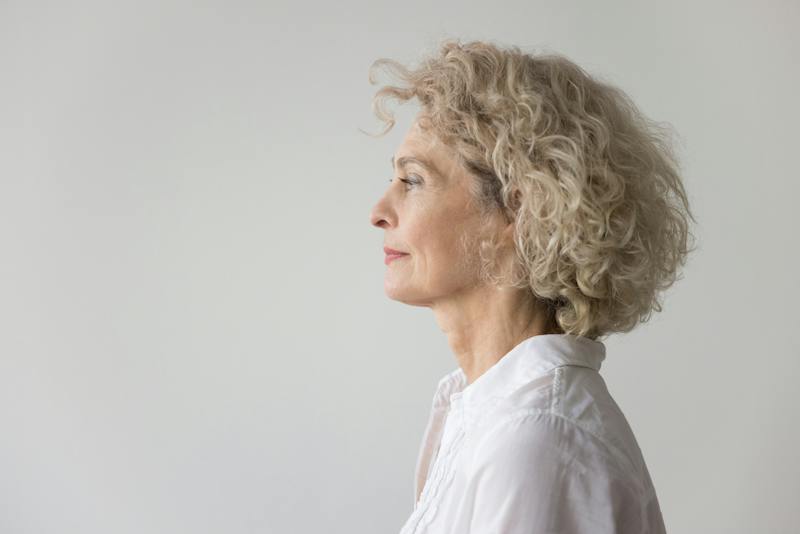 Side profile of a mature woman with curly blonde hair and a defined jawline and neck.