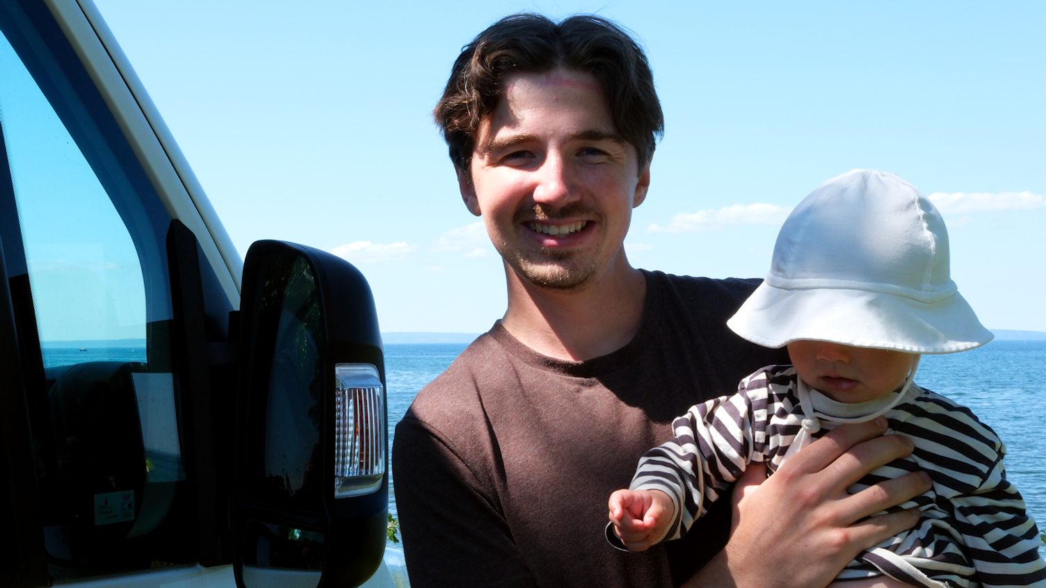 En pappa med sin bebis står vid deras van.