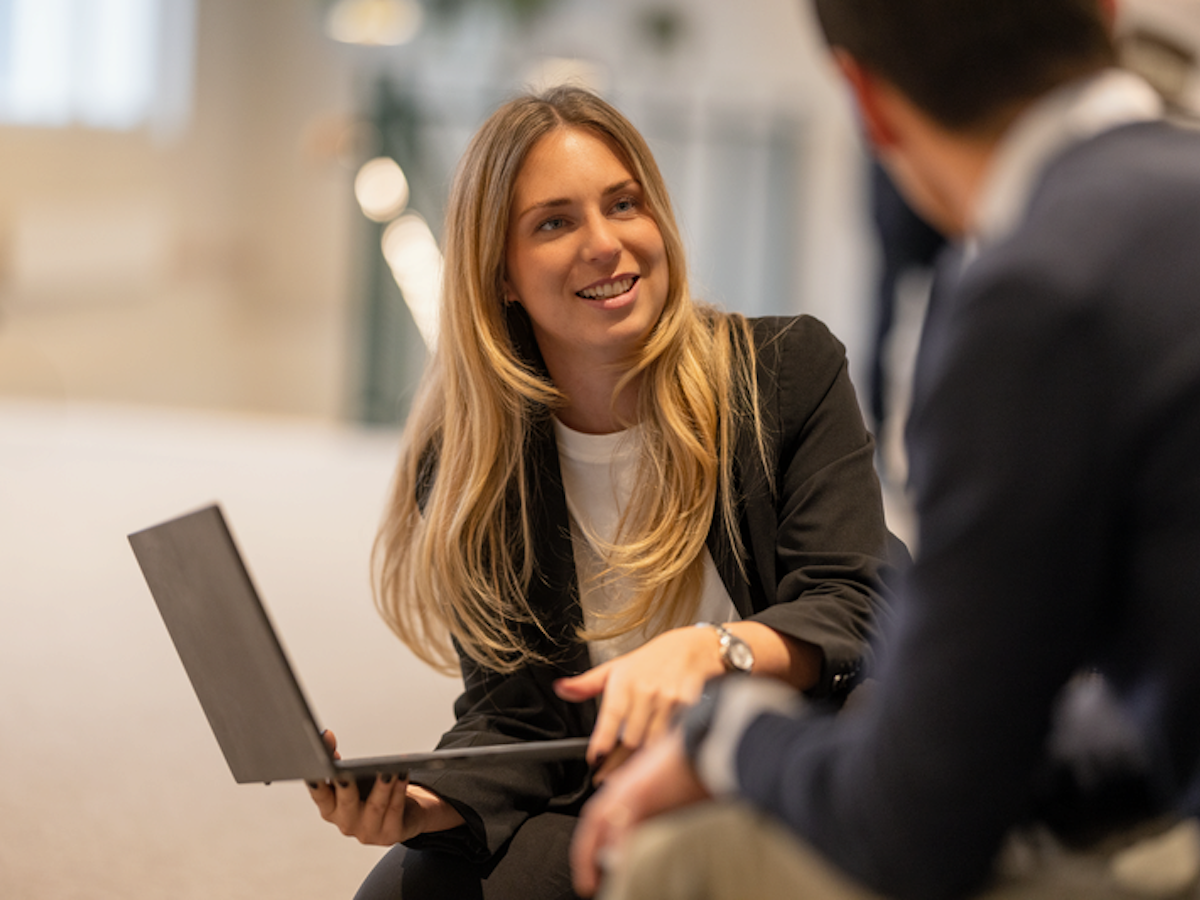 En kvinna håller i en laptop och pratar med en man