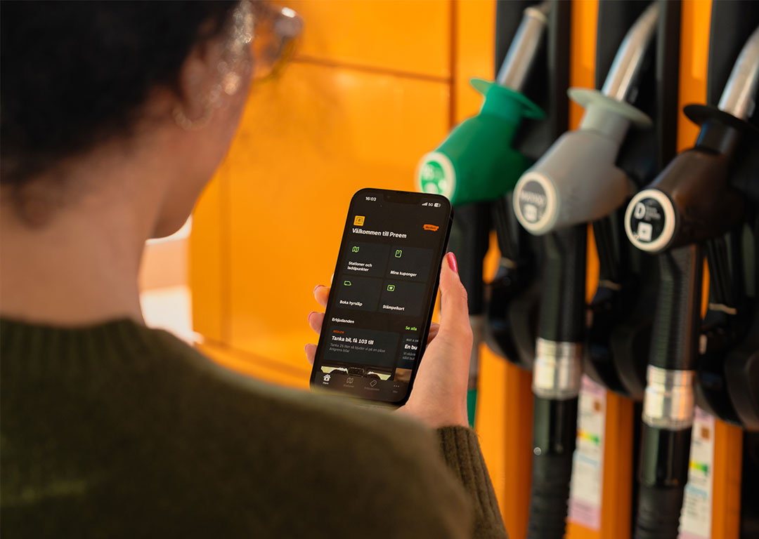 Kvinna står vid en bensinpump och använder Preems privatapp på sin telefon