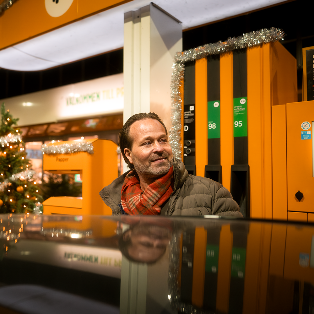 Glad man som tankar på en bensinstation i juletider