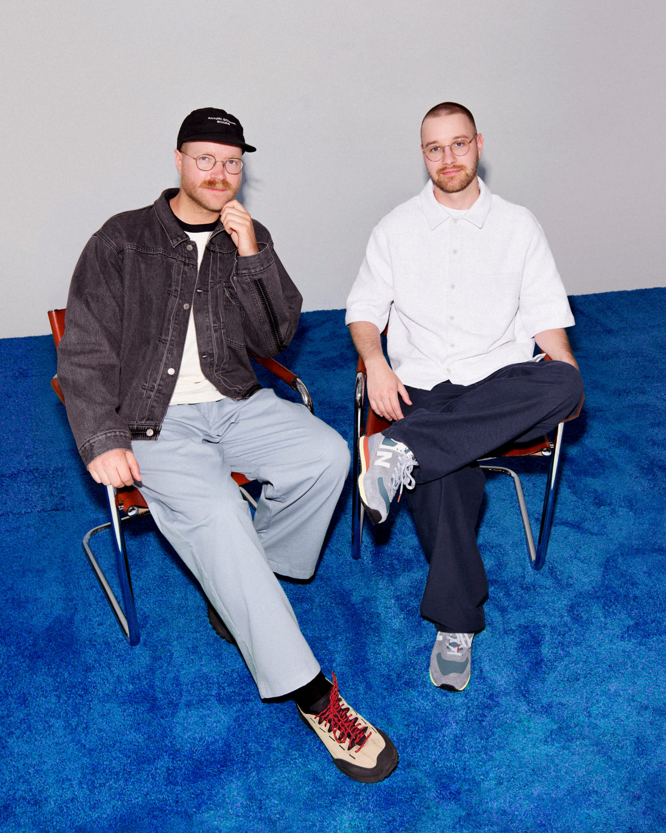 Portrait of Deven and Pier-Luc, founders of Domaine Public, seated on chairs against a blue backdrop