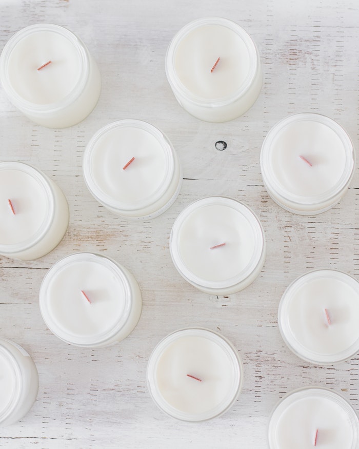 Top-down view of white soy candles in clear glass jars with wood wicks on a painted wood surface