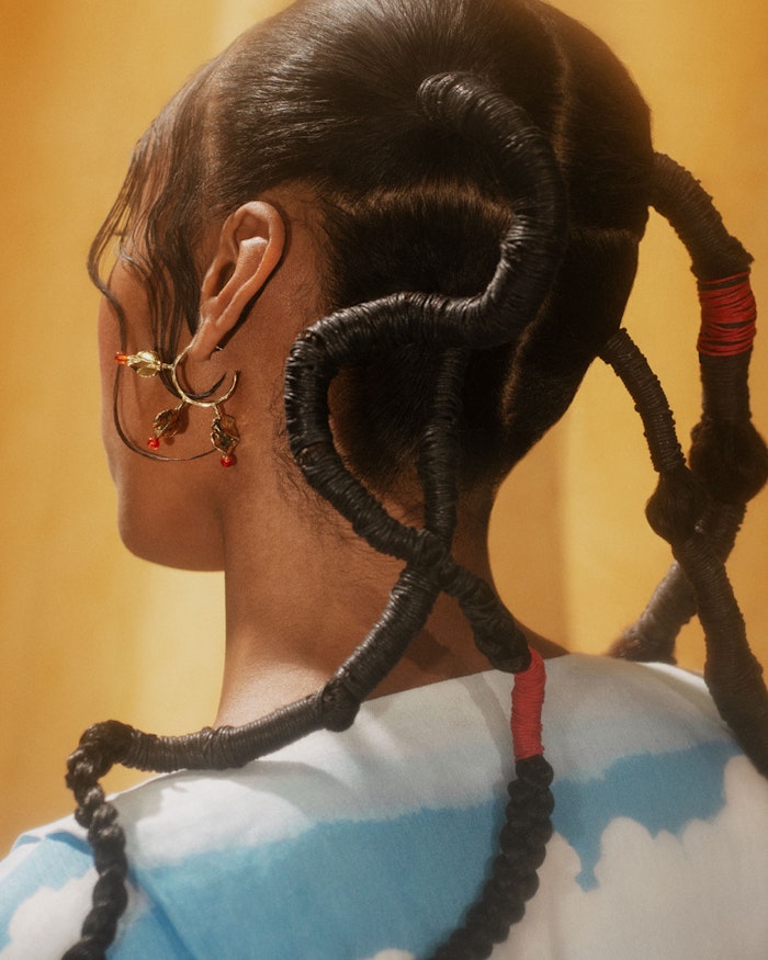 Close-up from behind of sculptural threaded hair with red accents and a dangling gold earring