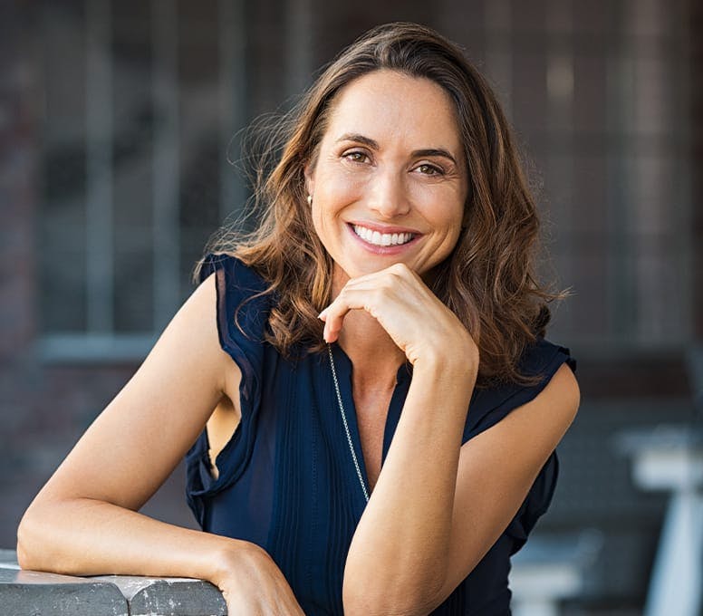 woman in dark blue dress smiling with hand on her chin