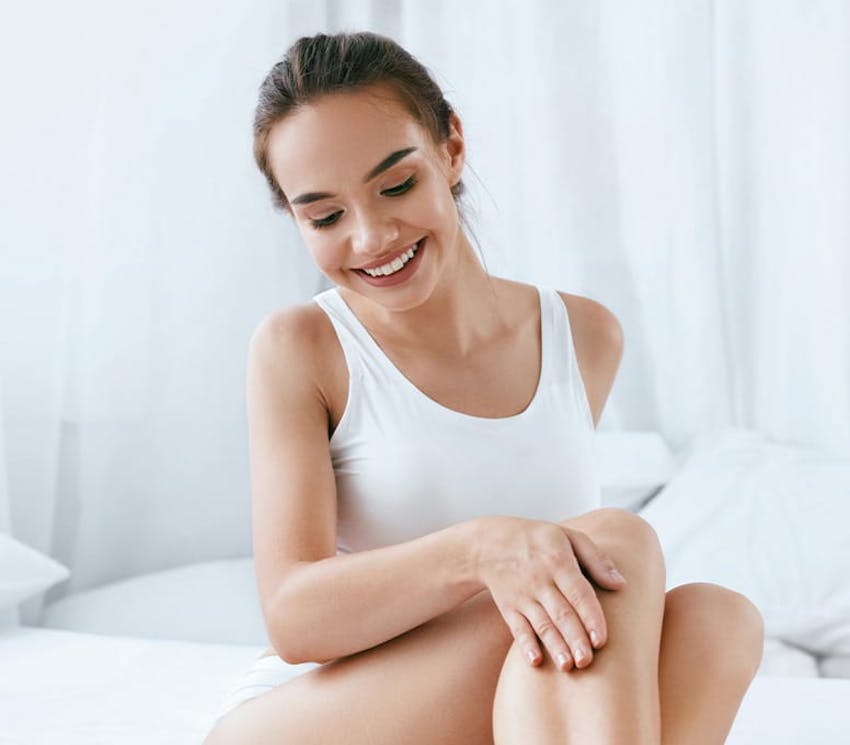 woman sitting on bed looking and touching at her legs