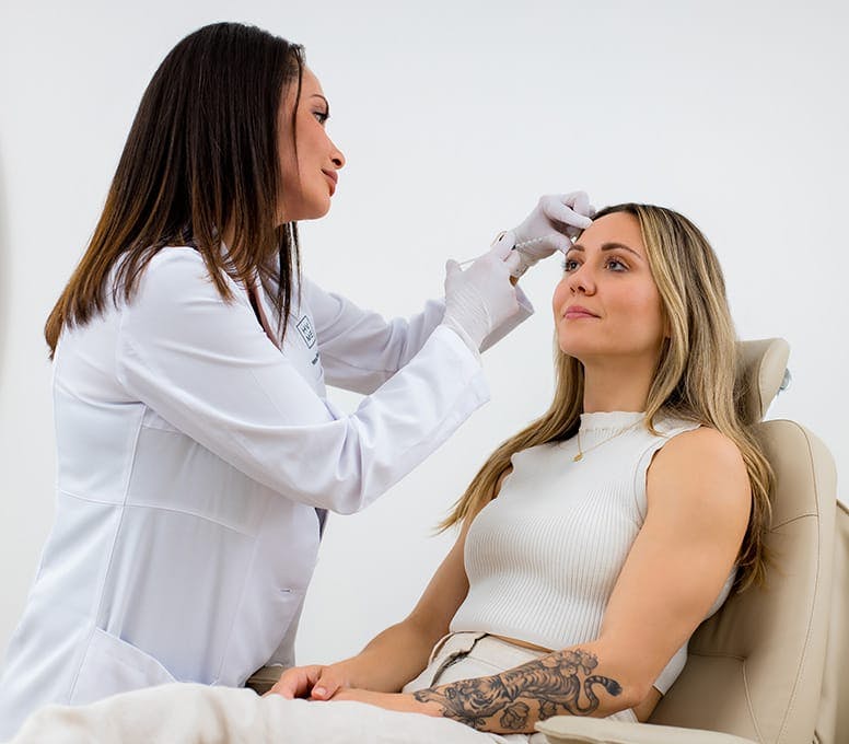 woman using a syringe against another woman's forehead