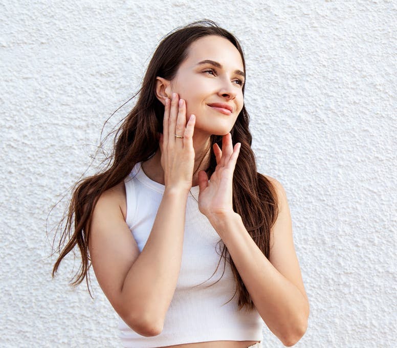woman outside against a white wall with her hands on her face