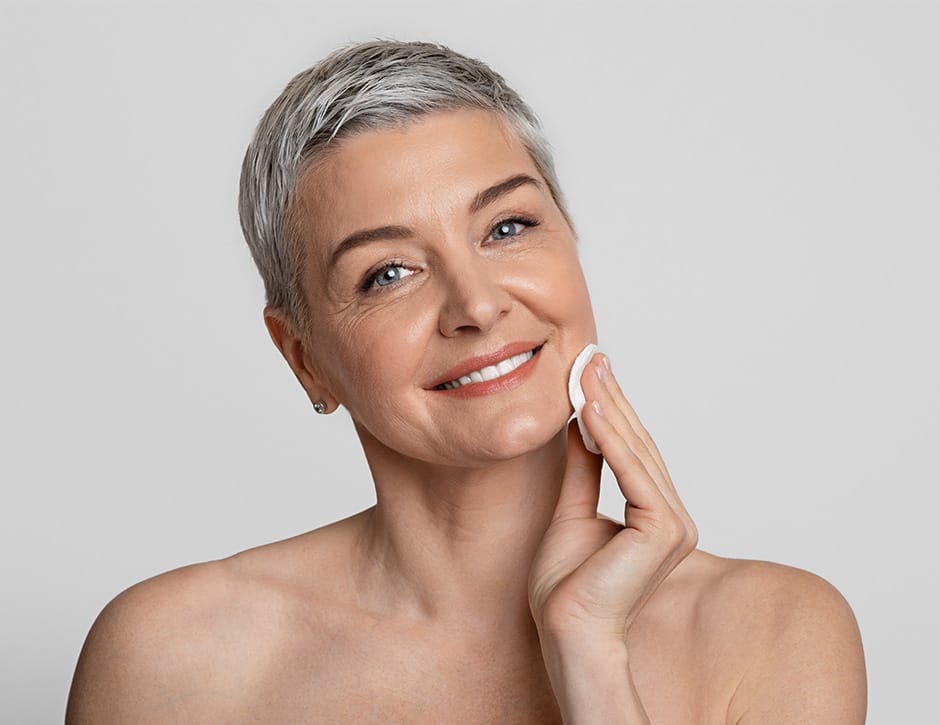 woman with short grey hair cleaning her face with a cotton round