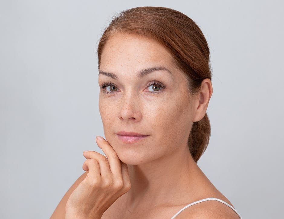 woman with red hair in a bun with her hand touching her chin