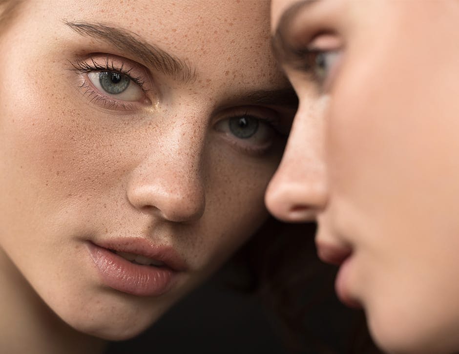 closeup of woman with freckles looking into a mirror