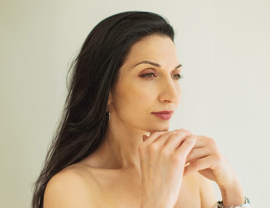 woman with black hair with both hands under her chin